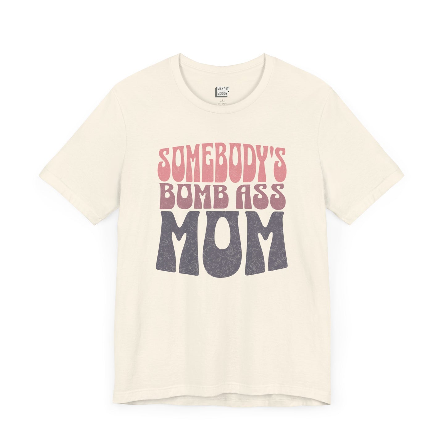 Off-white mom t-shirt featuring bold, retro-style text reading Somebody's Bomb Ass Mom in pink and grey.