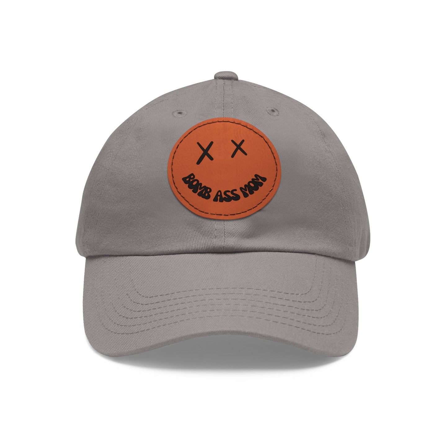 A Bomb Ass Mom Hat in grey featuring an orange patch with a smiling face and X eyes, plus "BOMB ASS MOM" text on the brim.