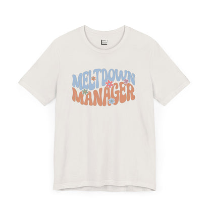 Vintage white colored mom t-shirt featuring the words MELTDOWN MANAGER in a colorful retro-style font with retro flower designs.