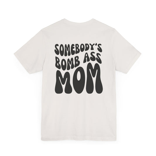 White mom t-shirt featuring bold black retro text on the back that reads SOMEBODY'S BOMB ASS MOM.