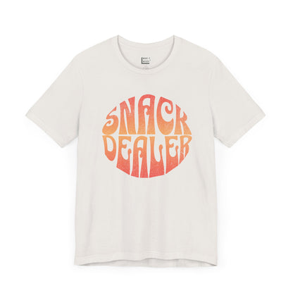 A vintage white mom t-shirt featuring a retro, orange gradient font with the words SNACK DEALER printed inside a circular design.