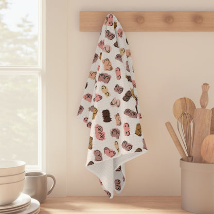 A Boobie Pattern Breastfeeding Towel hangs on a peg rack above a kitchen counter with bowls, cups, and wooden utensils.