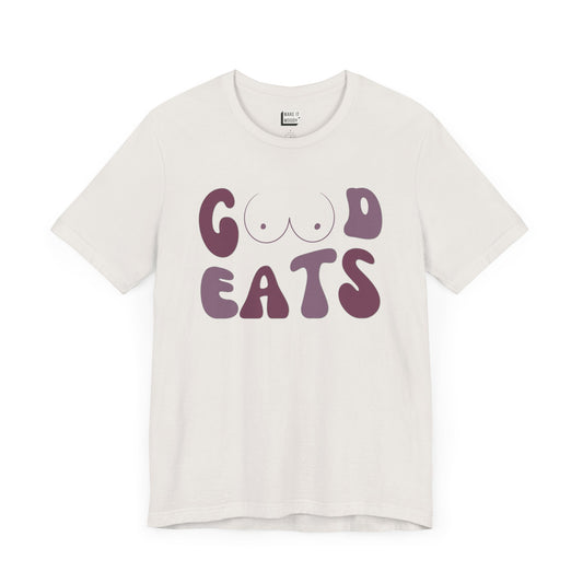 Vintage white retro-style breastfeeding t-shirt that says GOOD EATS on the front with a minimalistic breast graphic in place of the double O in the word GOOD.