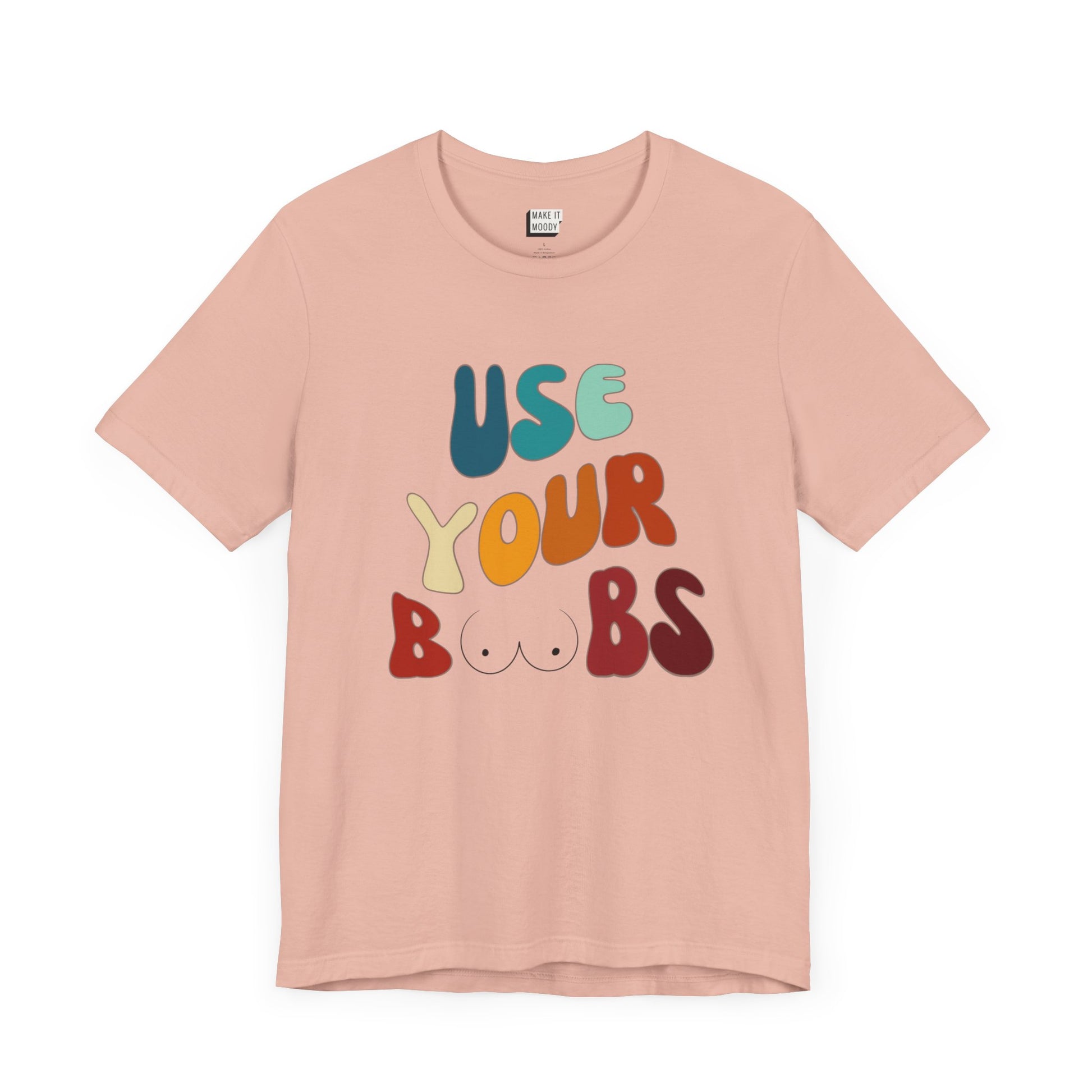 Peach colored Breastfeeding T-shirt that says USE YOUR BOOBS in multicolor retro lettering with a minimalistic breast graphic in place of the double O in the word BOOBS.