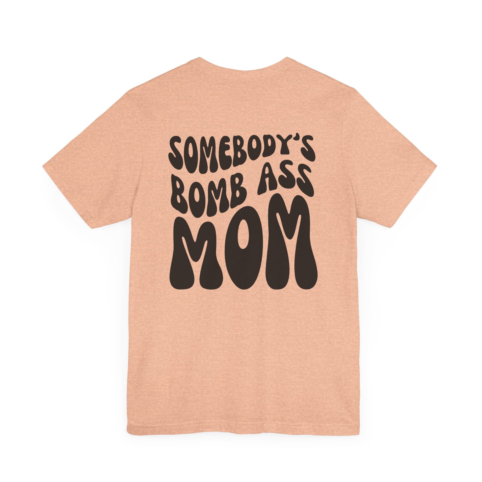 Heather peach mom t-shirt featuring bold black retro text on the back that reads SOMEBODY'S BOMB ASS MOM.