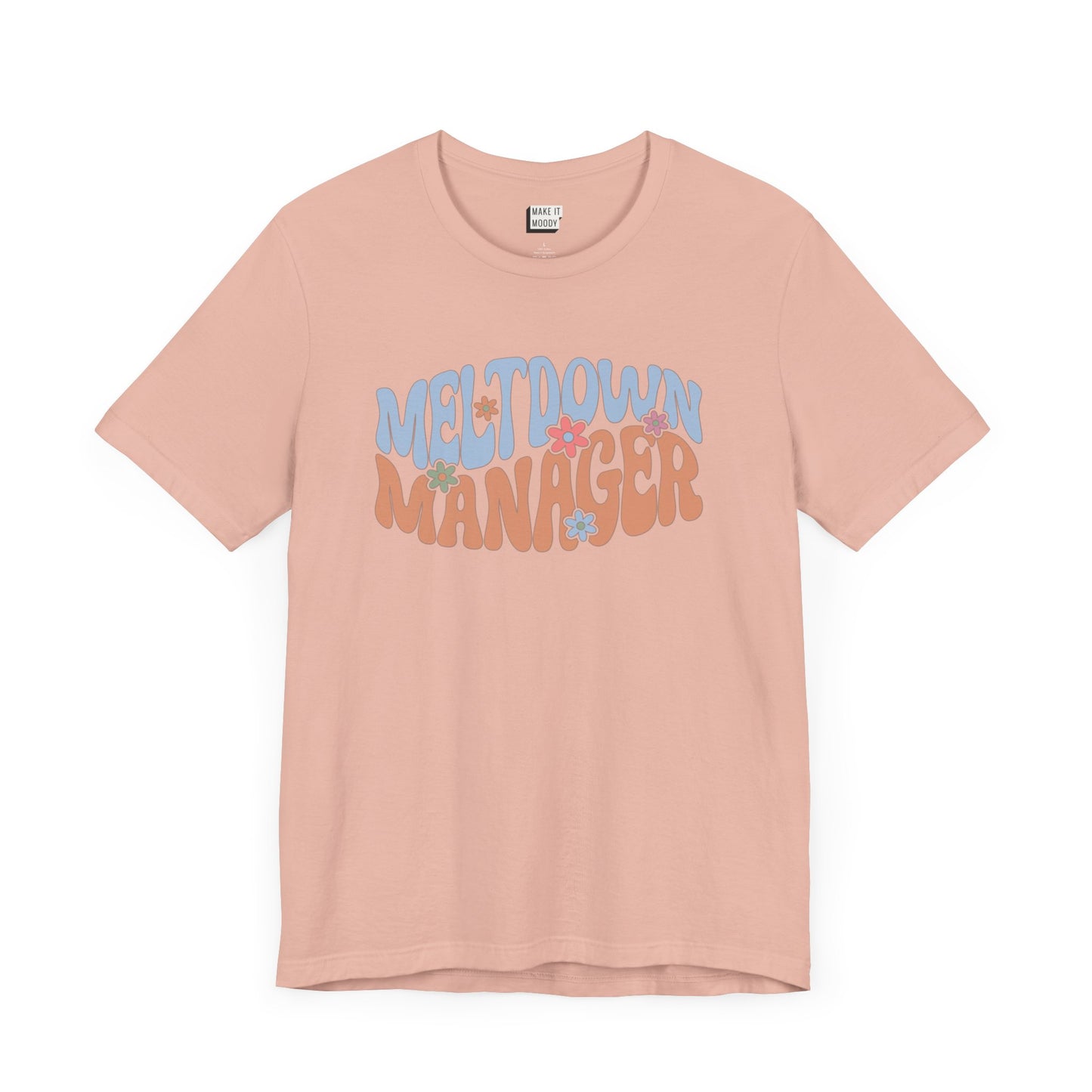 Peach colored mom t-shirt featuring the words MELTDOWN MANAGER in a colorful retro-style font with retro flower designs.