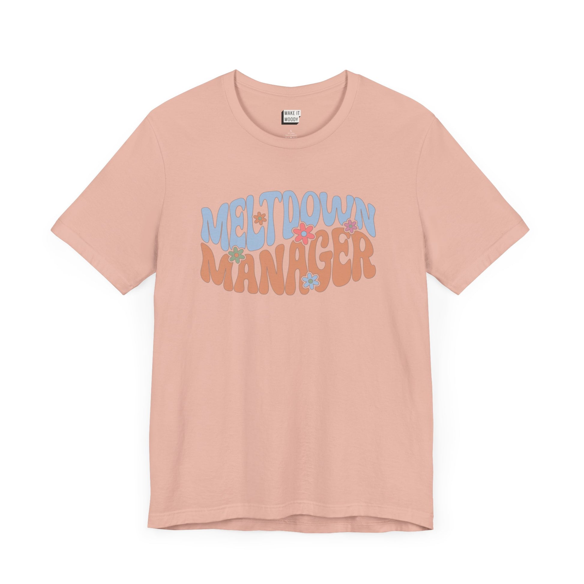 Peach colored mom t-shirt featuring the words MELTDOWN MANAGER in a colorful retro-style font with retro flower designs.