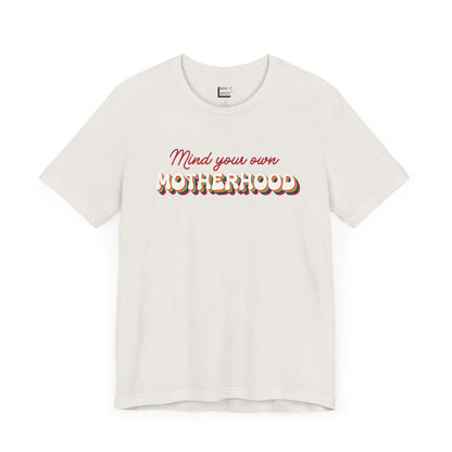 Off-white mom t-shirt featuring the text Mind your own MOTHERHOOD in red and rainbow-colored 3D-style retro letters.