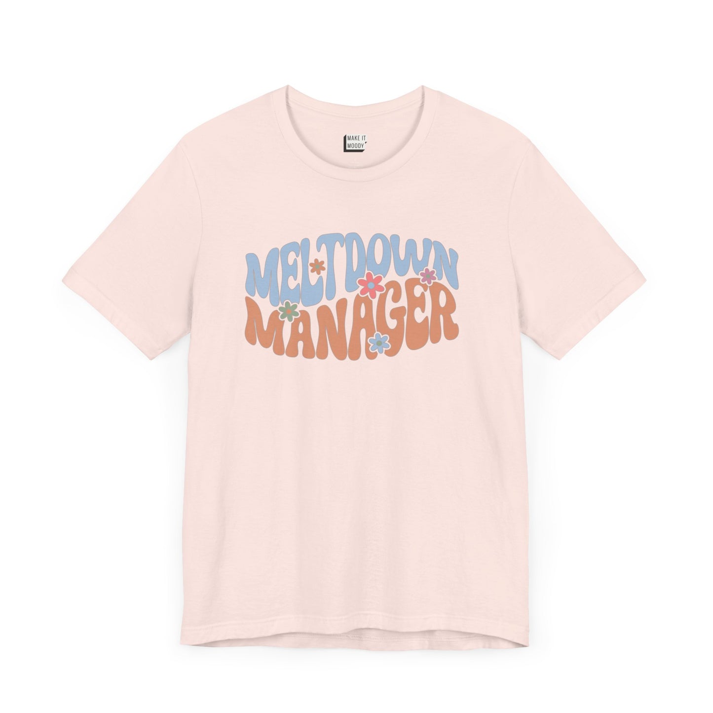 Soft pink colored mom t-shirt featuring the words MELTDOWN MANAGER in a colorful retro-style font with retro flower designs.