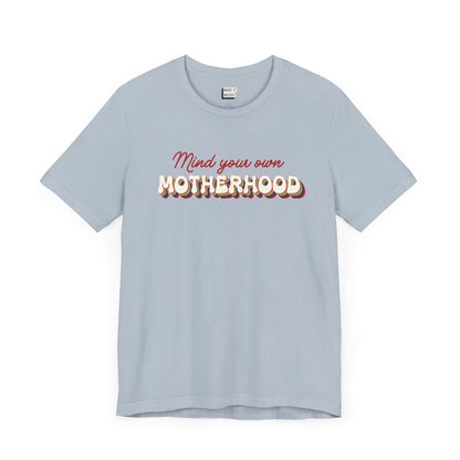 Light blue mom t-shirt featuring the text Mind your own MOTHERHOOD in red and rainbow-colored 3D-style retro letters.