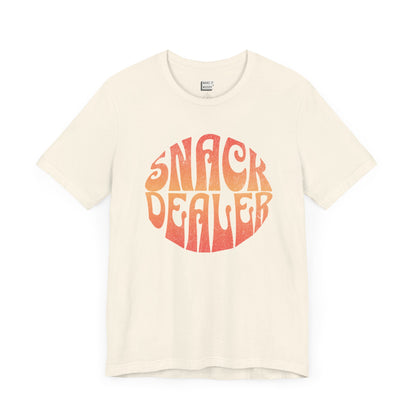 An off-white mom t-shirt featuring a retro, orange gradient font with the words SNACK DEALER printed inside a circular design.