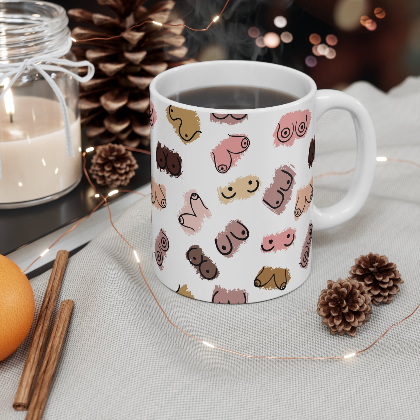 The Boobie Pattern Breastfeeding Mug 11oz, featuring a vibrant animal design, is filled with a dark liquid and placed next to pine cones, a candle, an orange, and cinnamon sticks. It’s perfect for a breastfeeding mom seeking a cozy moment.