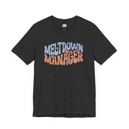 Dark heather grey colored mom t-shirt featuring the words MELTDOWN MANAGER in a colorful retro-style font with retro flower designs.