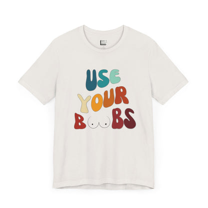 Vintage white Breastfeeding T-shirt that says USE YOUR BOOBS in multicolor retro lettering with a minimalistic breast graphic in place of the double O in the word BOOBS.
