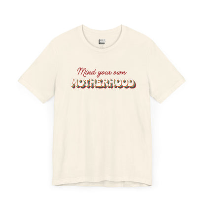 Off-white mom t-shirt featuring the text Mind your own MOTHERHOOD in red and rainbow-colored 3D-style retro letters.