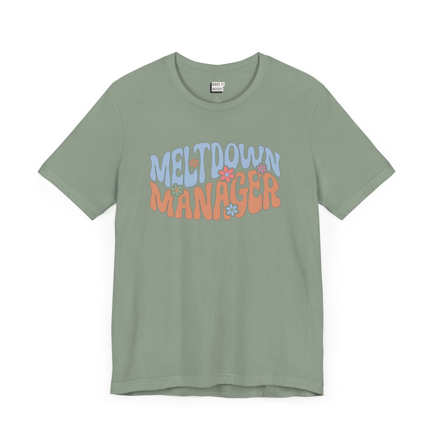 Sage green colored mom t-shirt featuring the words MELTDOWN MANAGER in a colorful retro-style font with retro flower designs.