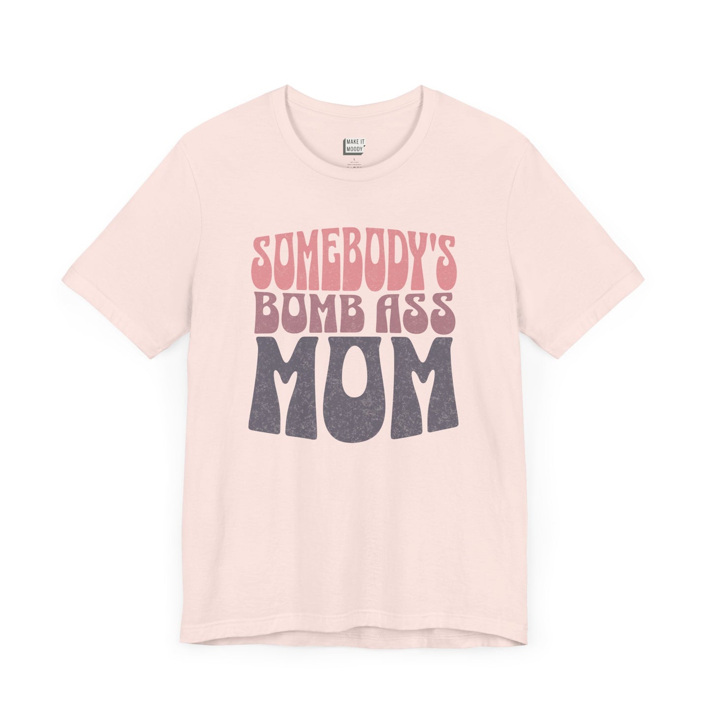 Light pink mom t-shirt featuring bold, retro-style text reading Somebody's Bomb Ass Mom in pink and grey.